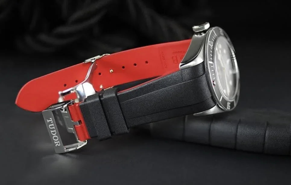 Bracelet de montre Tudor noir et rouge en caoutchouc, accessoire de luxe sur fond noir.