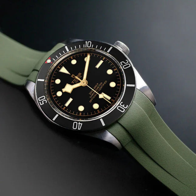Montre de luxe avec bracelet vert en caoutchouc, cadran noir et boîtier en acier sur fond sombre.
