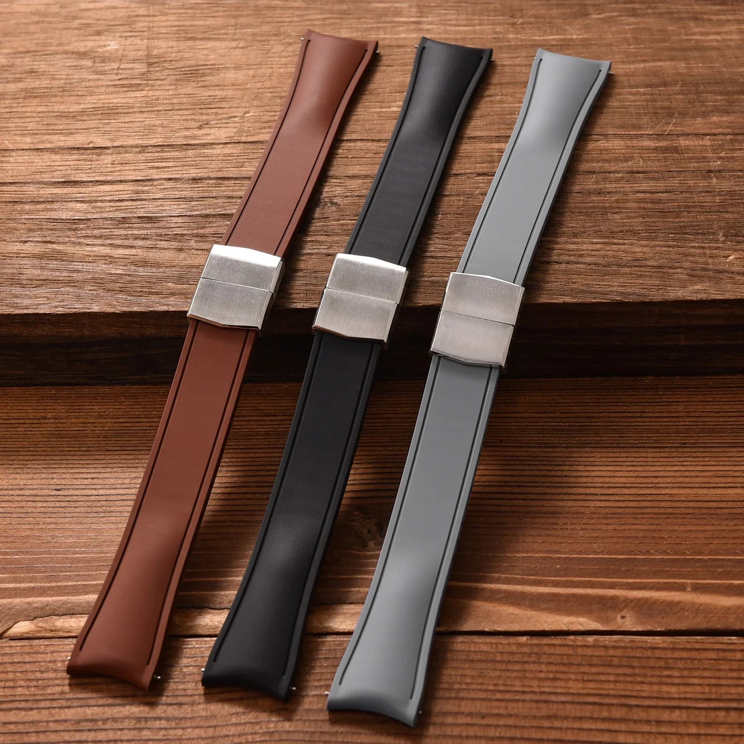 Trois bracelets de montre luxe en cuir marron, noir et gris avec boucle argent, sur bois