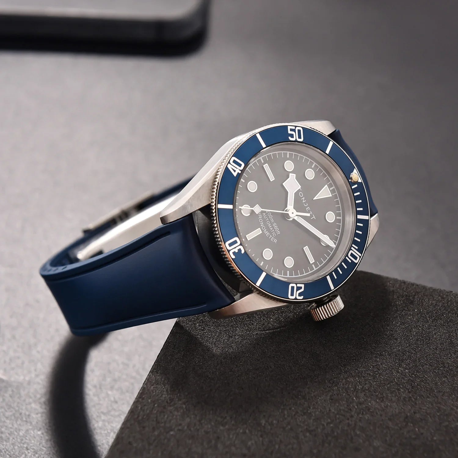 Montre de luxe avec bracelet bleu, lunette bleu, cadran noir posée sur une surface sombre
