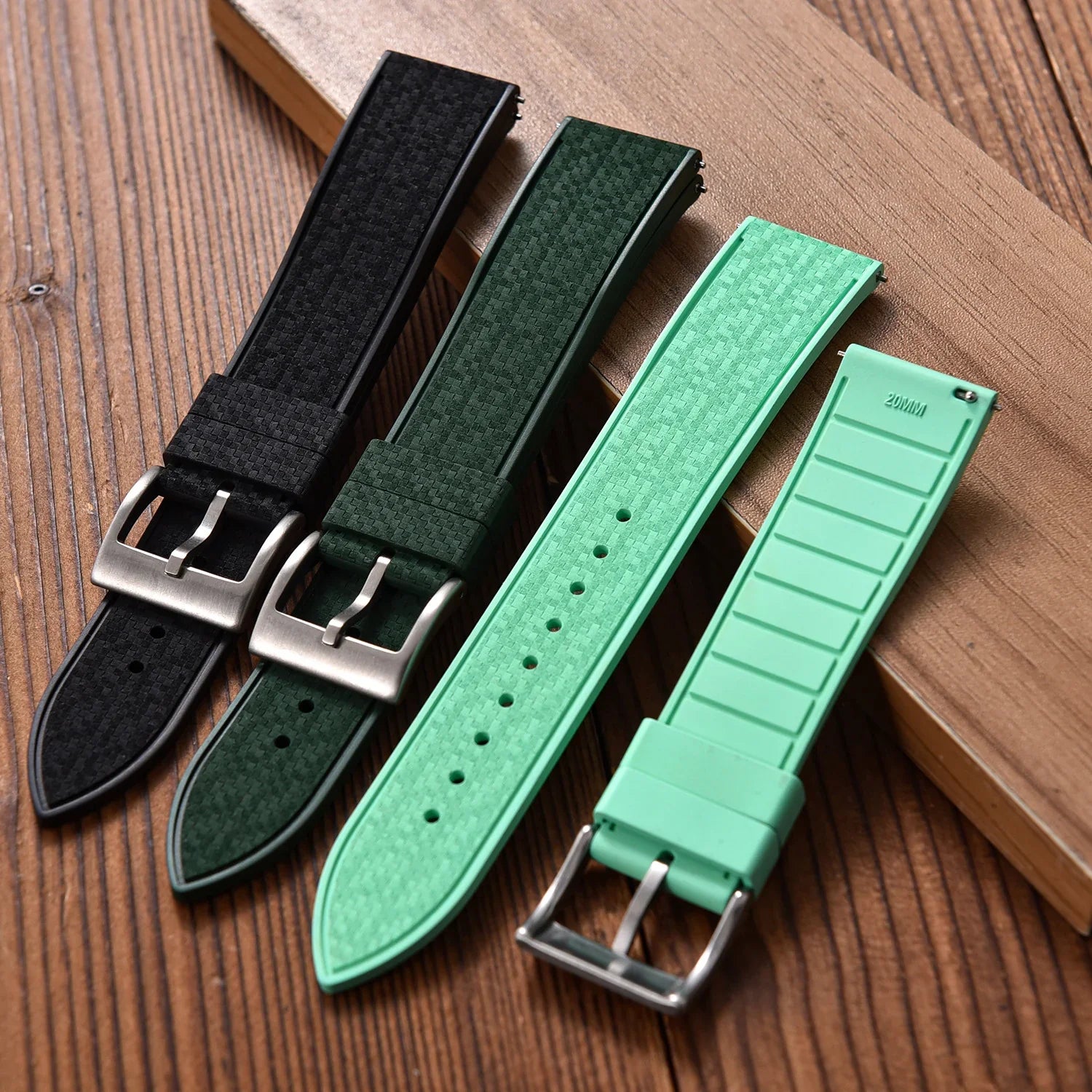 Trois bracelets de montre en cuir et caoutchouc noir, vert et vert clair sur table bois