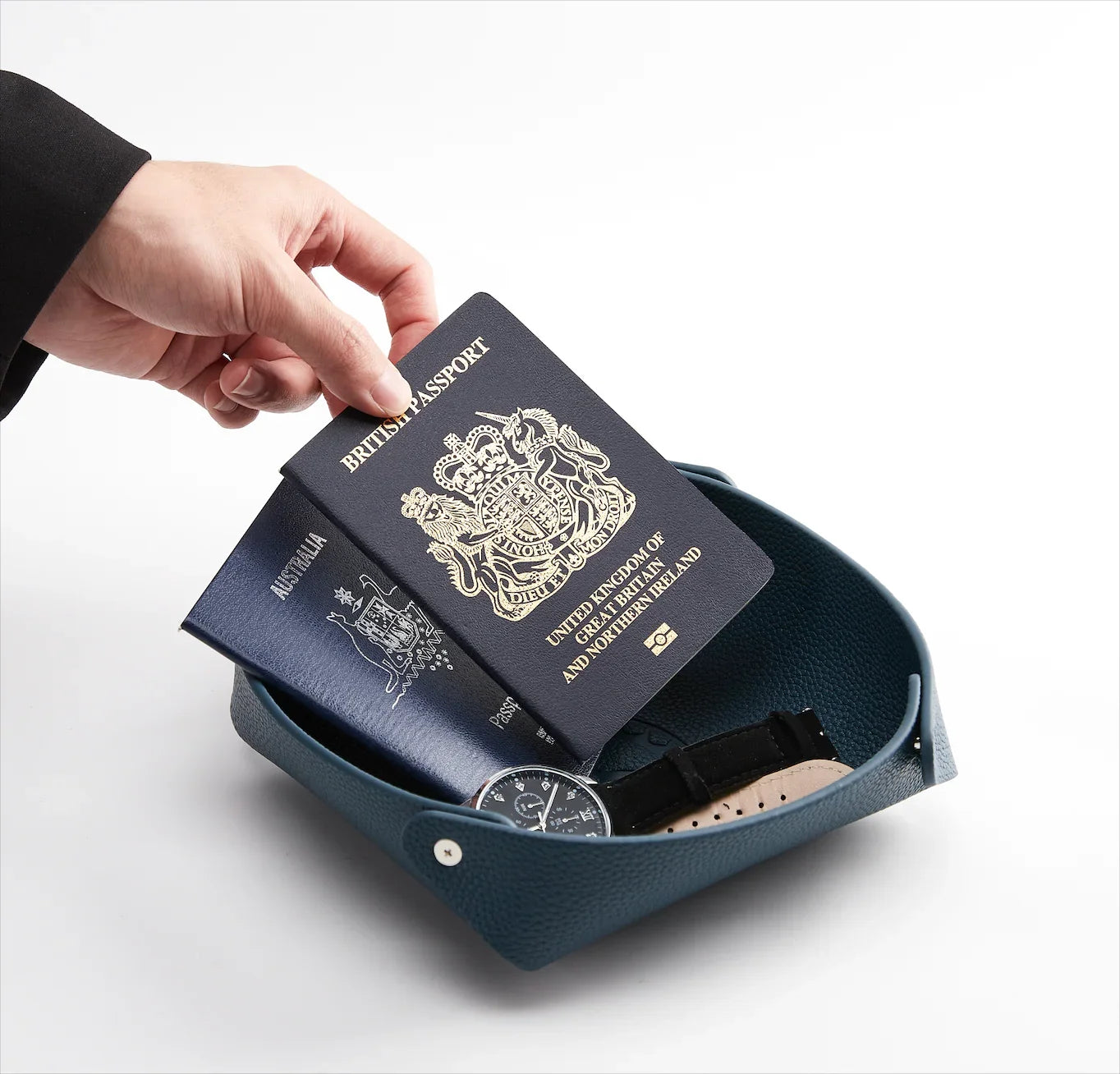 Main tenant un passeport britannique dans un vide-poche en cuir avec montre de luxe, accessoires voyage.